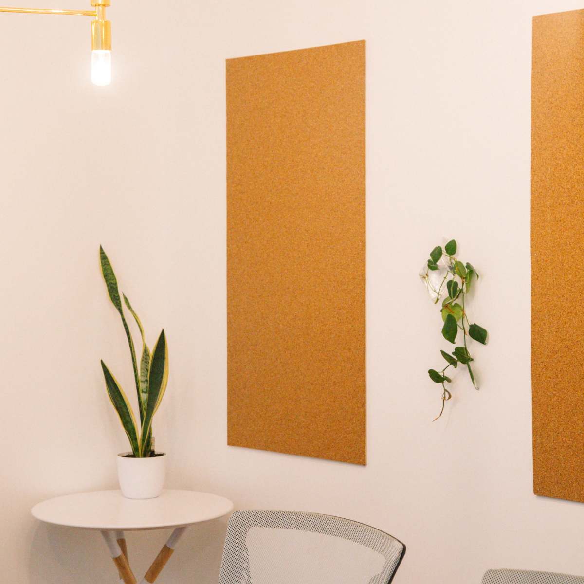 A minimalistic meeting room with a round white table, a plant in a pot, cork boards on the walls, and pendant lights hanging from the ceiling.