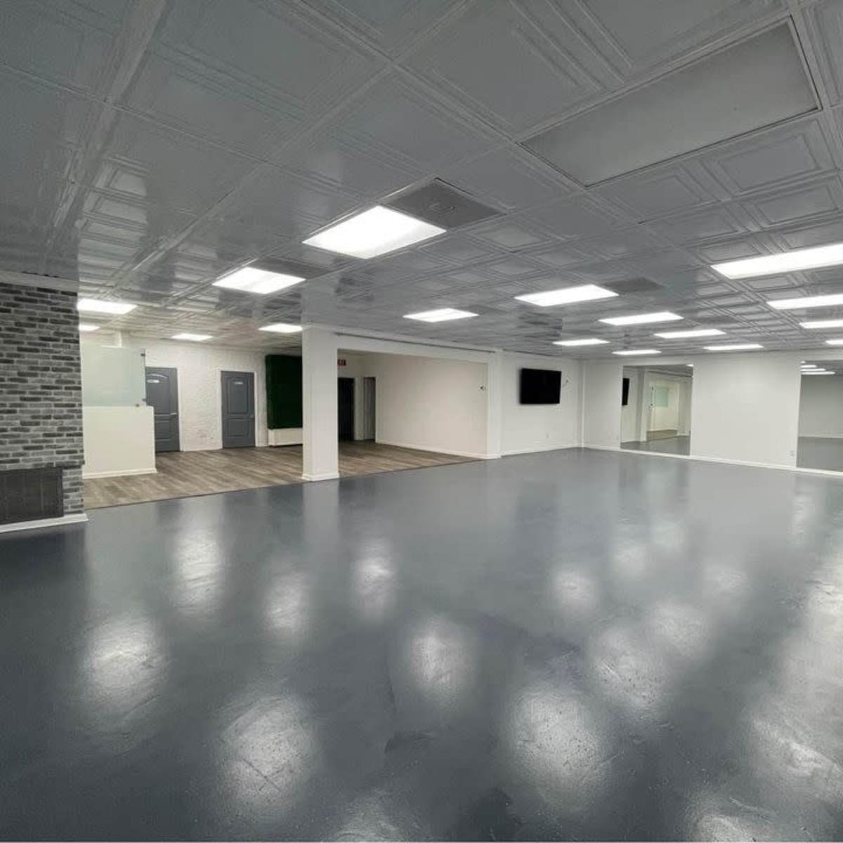 A spacious, empty room with a polished floor, bright ceiling lights, and large windows.