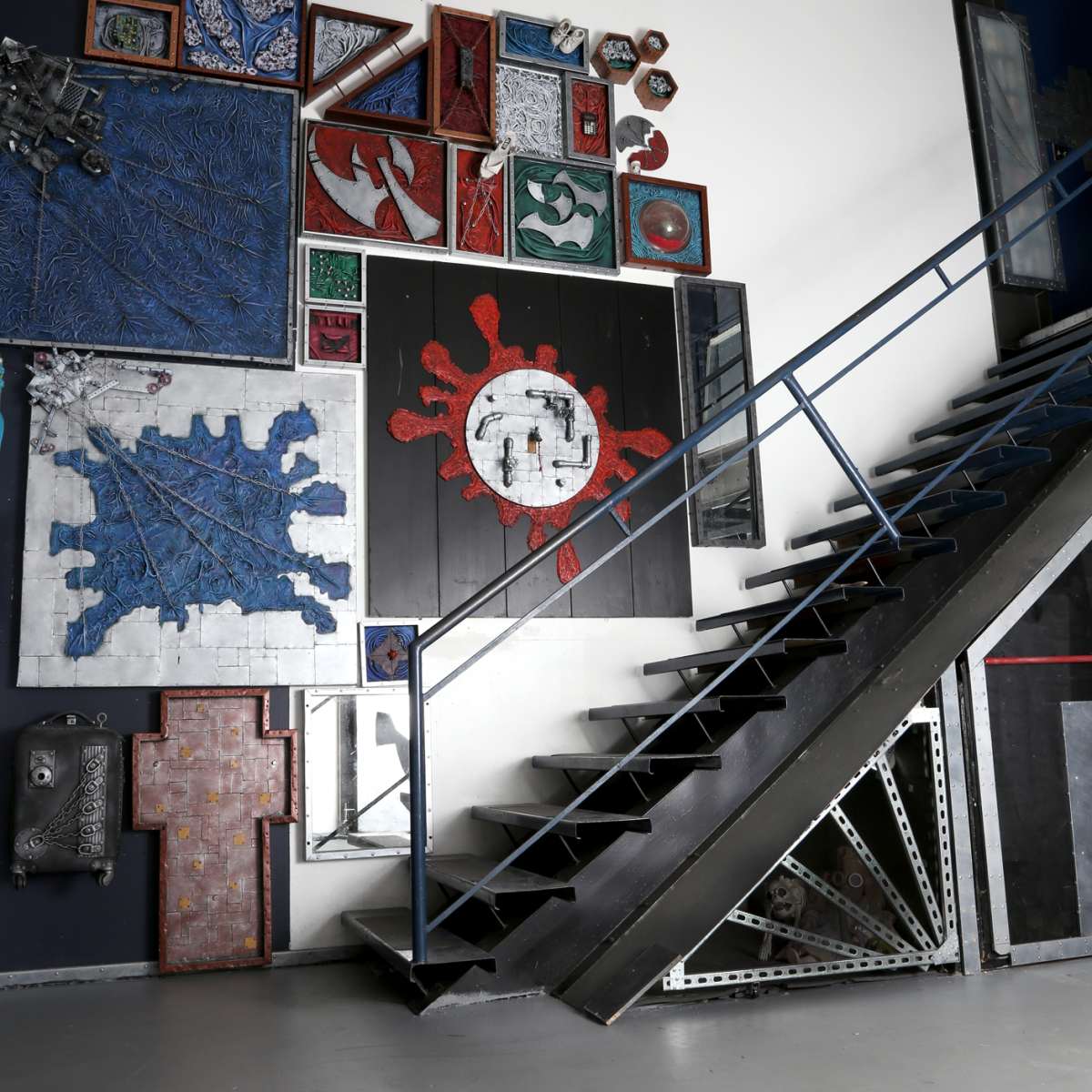 A metal staircase leads to an upper level beside a wall adorned with various colorful artworks and frames.