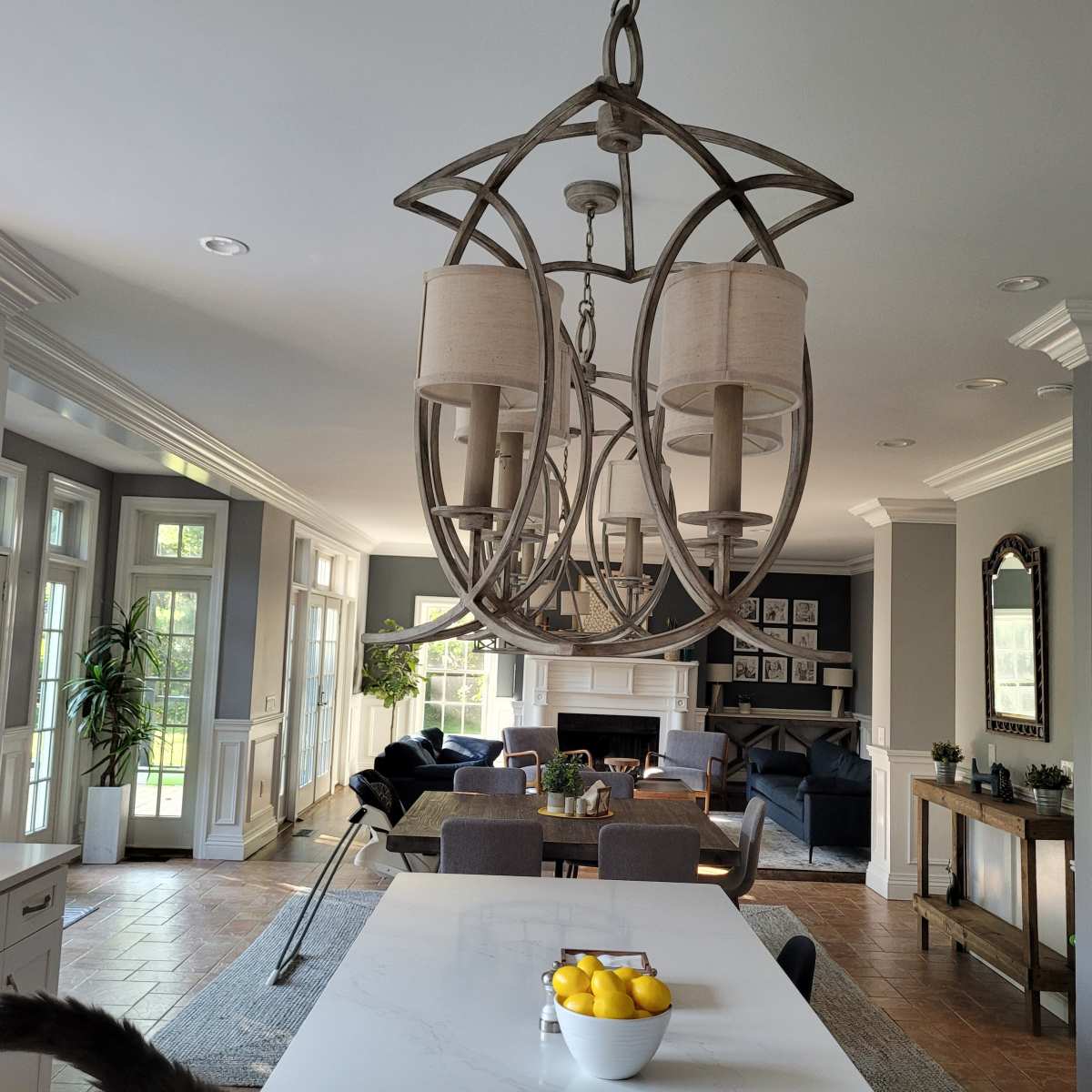 A spacious kitchen features a large island with a bowl of lemons, pendant lighting, and an open view of a living area with a fireplace and seating.