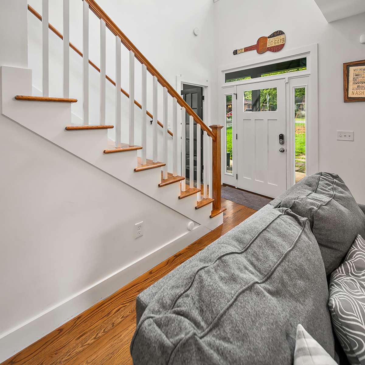 A well-lit entryway featuring a staircase with wooden steps, a front door with a window, and a gray couch in the foreground.