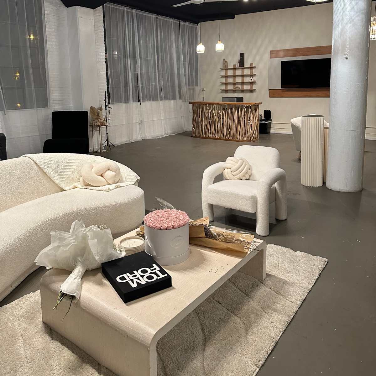 A modern, minimalist lounge area featuring a light-colored sofa, a coffee table with decorative items, and a wooden bar in the background, all under soft lighting.