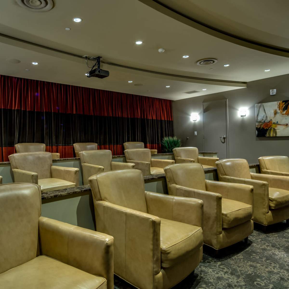 A small home theater with plush, beige leather seating arranged in rows against a dark, curtained backdrop.
