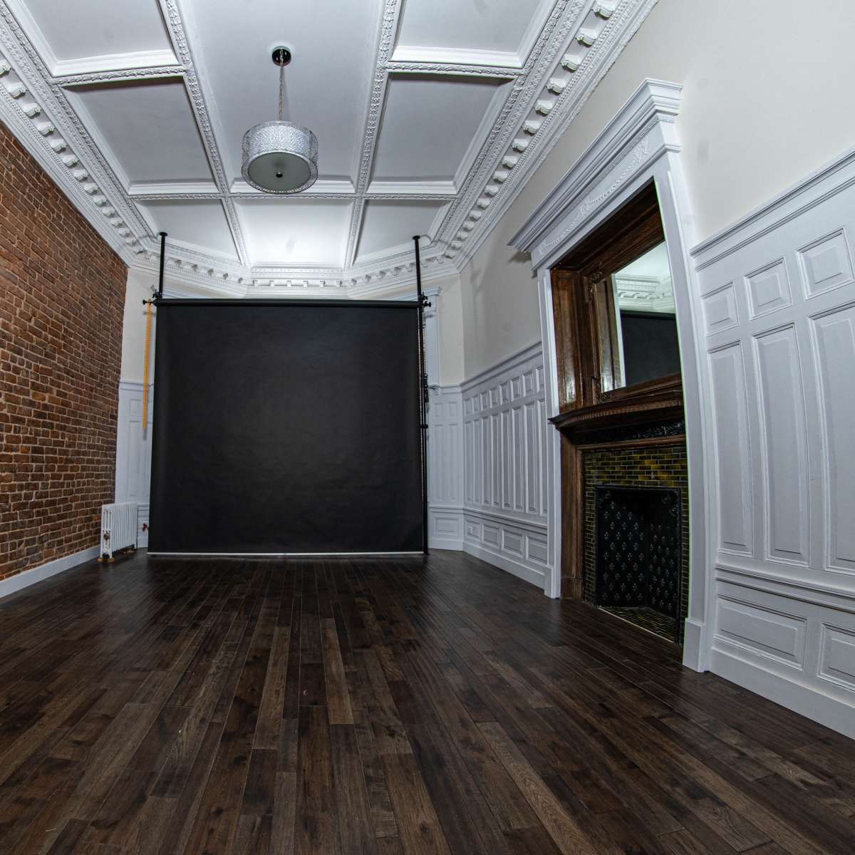 A spacious room with a brick wall, a dark backdrop, and a mirror framed by elegant moldings.