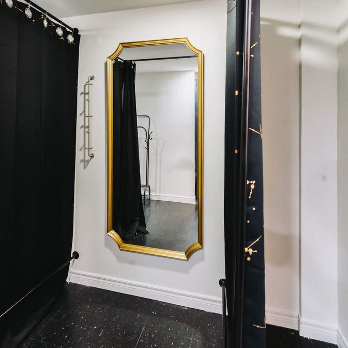 A dressing area with black curtain dividers and a large, ornate mirror on the wall.