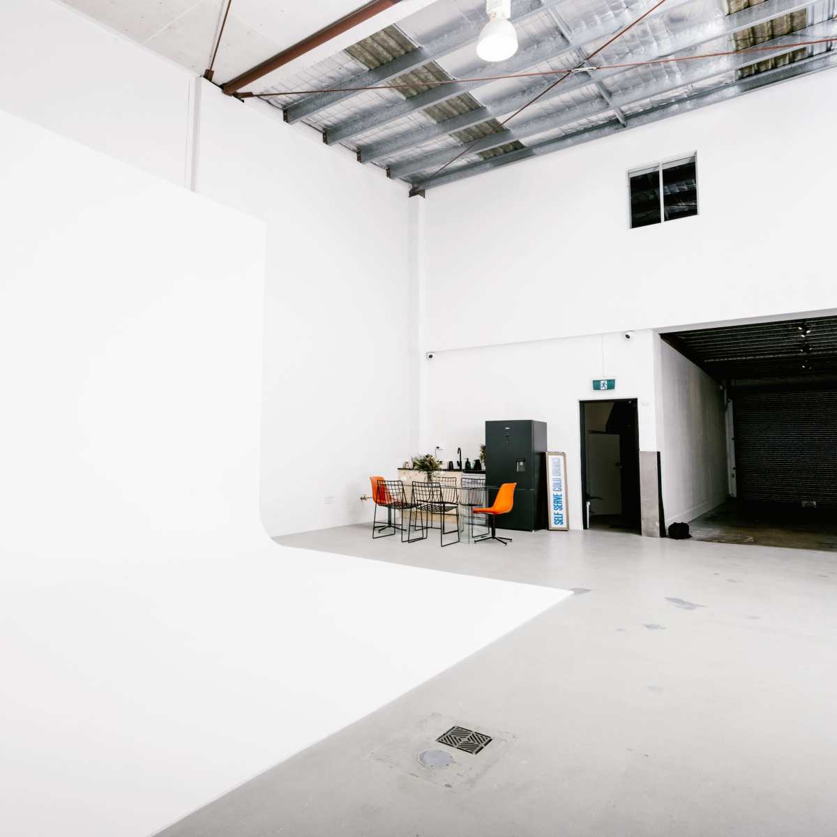 A spacious studio with a large white backdrop, a table set with chairs, and storage cabinets against the walls.