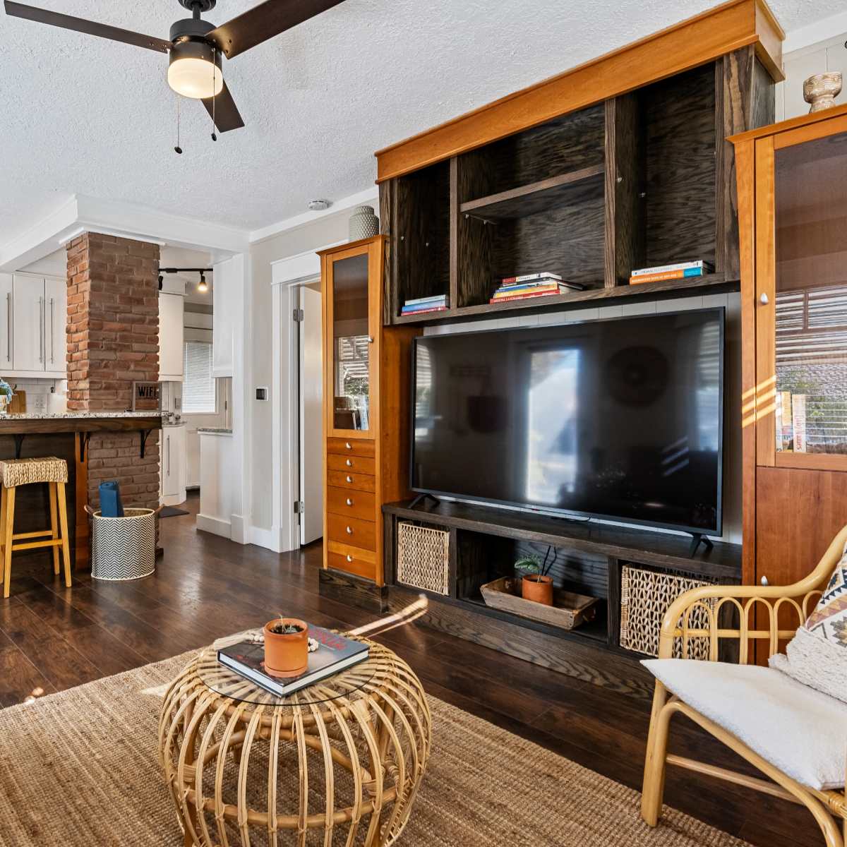 A modern living room featuring a television unit, a cozy seating area, and a kitchen bar with stools in the background.