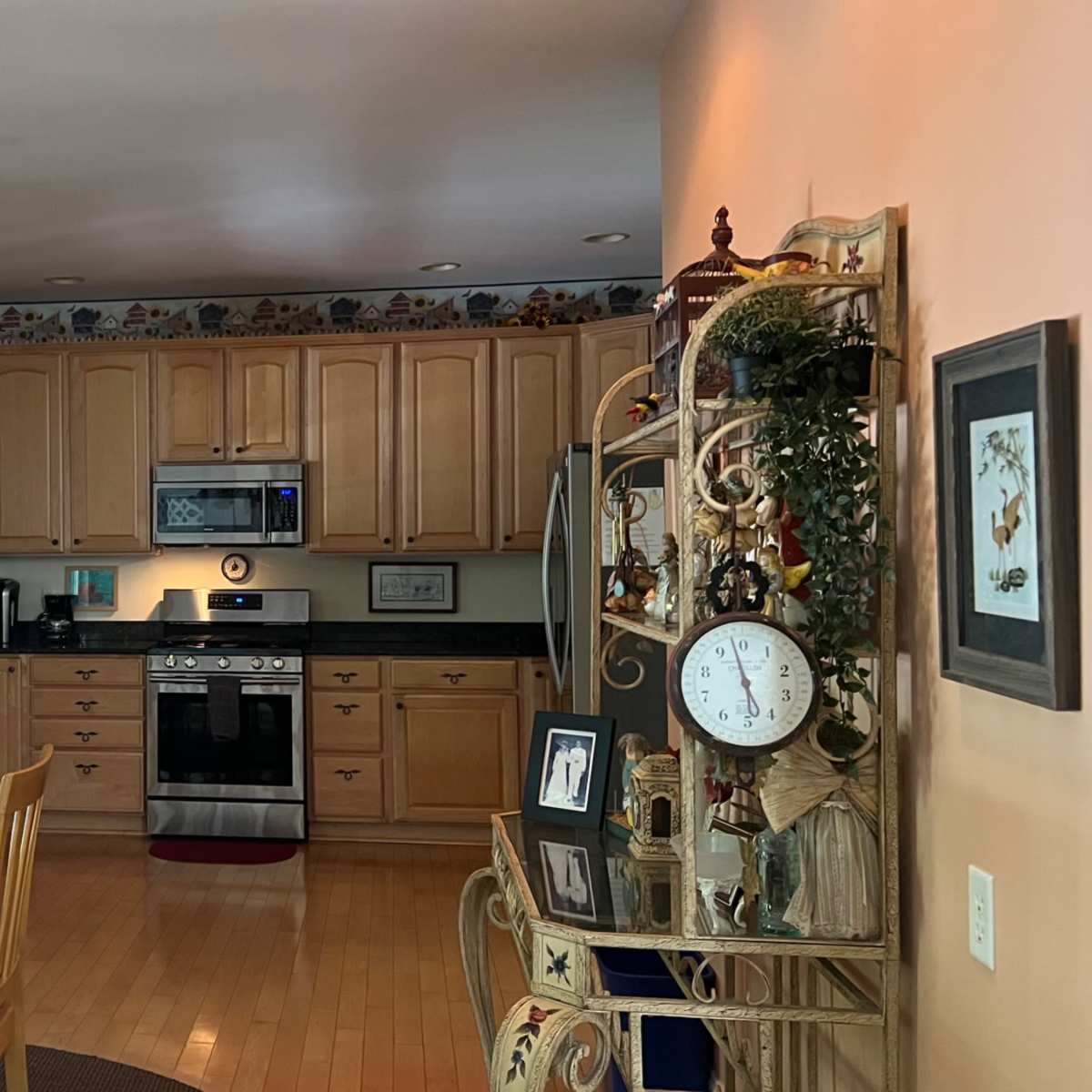 A spacious kitchen with wooden cabinets, stainless steel appliances, a central island, a dining table covered with a patterned tablecloth, and decorative shelving.