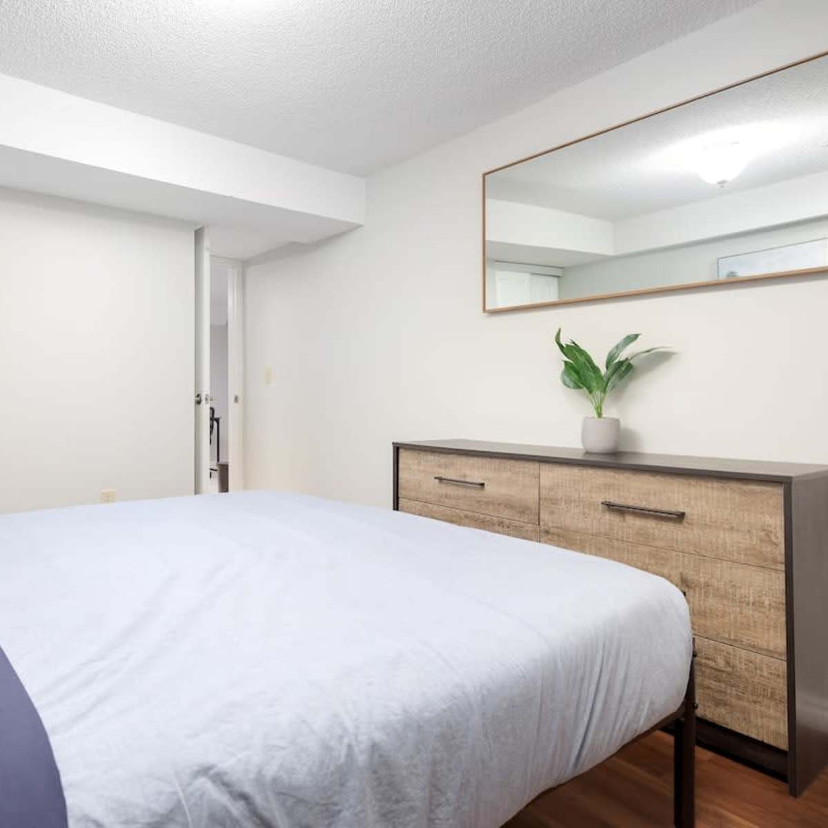 A neatly arranged bedroom featuring a bed with light blue bedding, a wooden dresser, and a mirror on the wall.