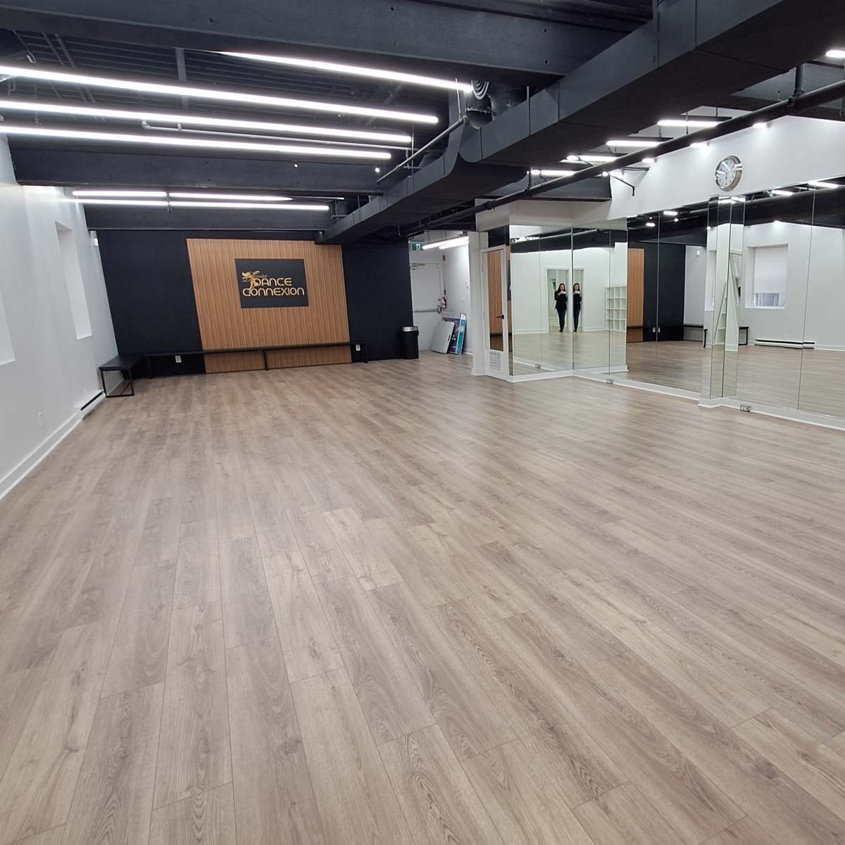 A spacious, empty studio with wooden flooring, large mirrors on one wall, and a reception area at the back.