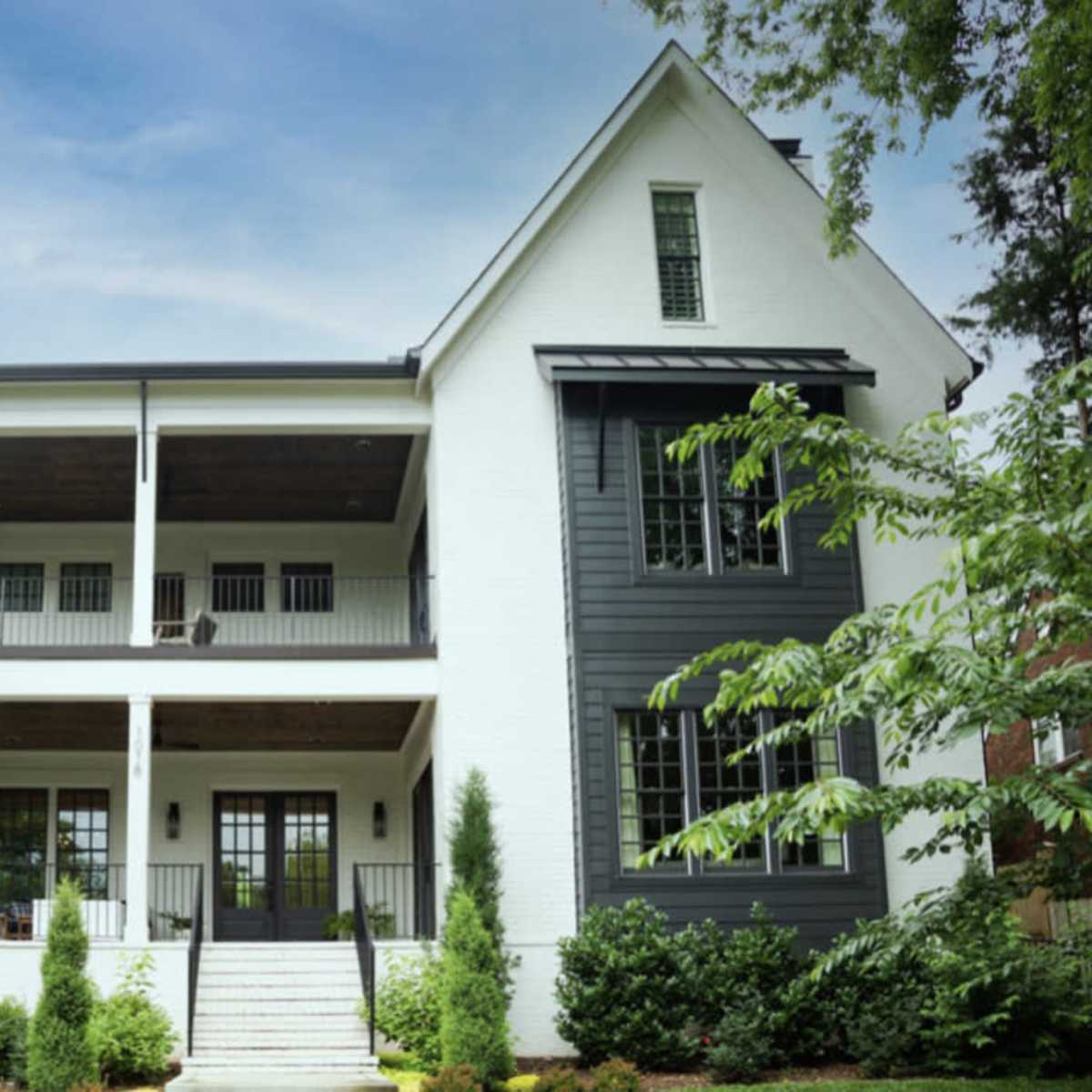 A modern three-story house features a white exterior with dark accents and a spacious porch.