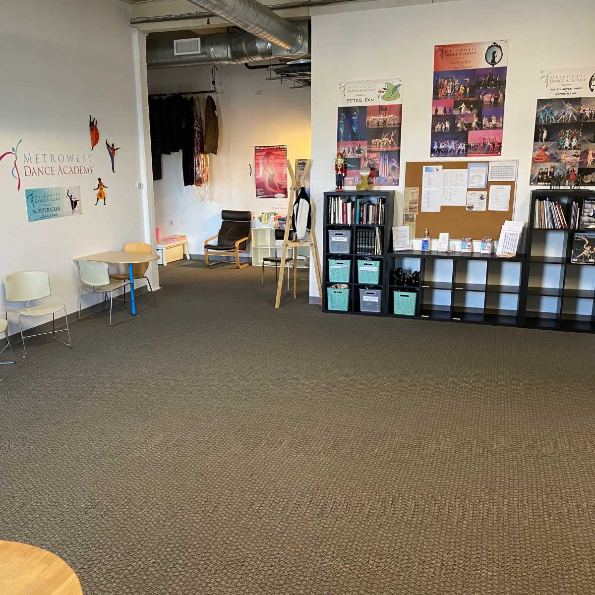 An empty dance studio with a seating area, posters on the walls, and storage shelves filled with supplies.