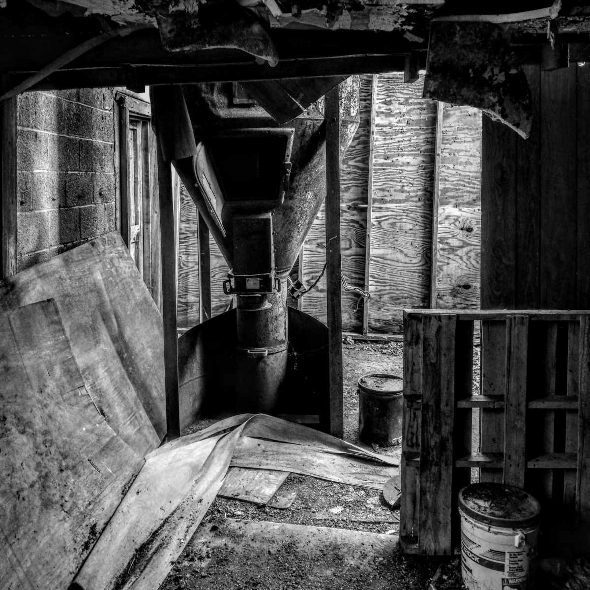 An industrial area features a large, rusty machine under a peeling ceiling with wooden pallets and scattered debris on the floor.