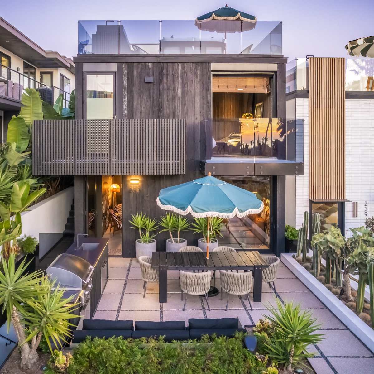 A modern house with a rooftop terrace and a patio area surrounded by various plants and outdoor furniture.