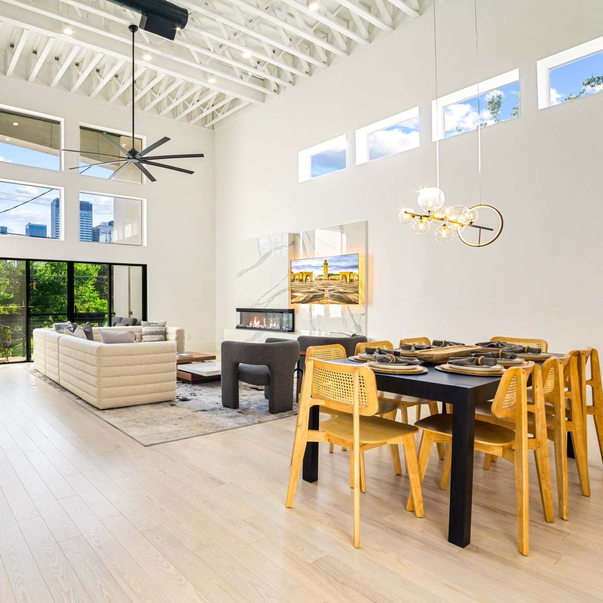 A modern living space with a dining area, plush seating, large windows, and a sleek staircase.