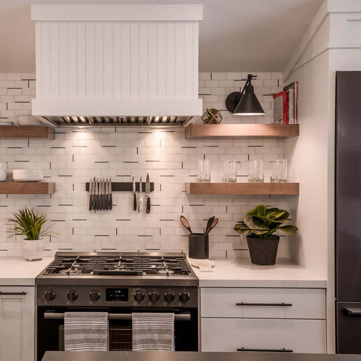 The kitchen features a wide stove beneath a hood, flanked by open shelves displaying dishware and plants against a tiled backsplash.