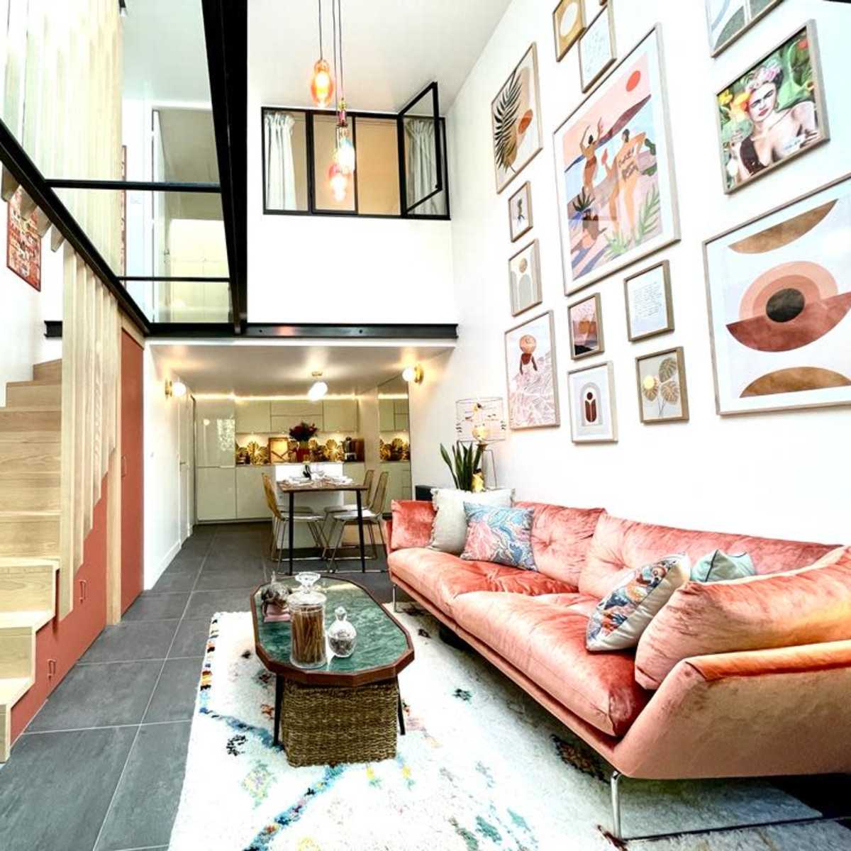 A modern living room with a coral sofa, a large staircase, and walls decorated with various framed artworks.