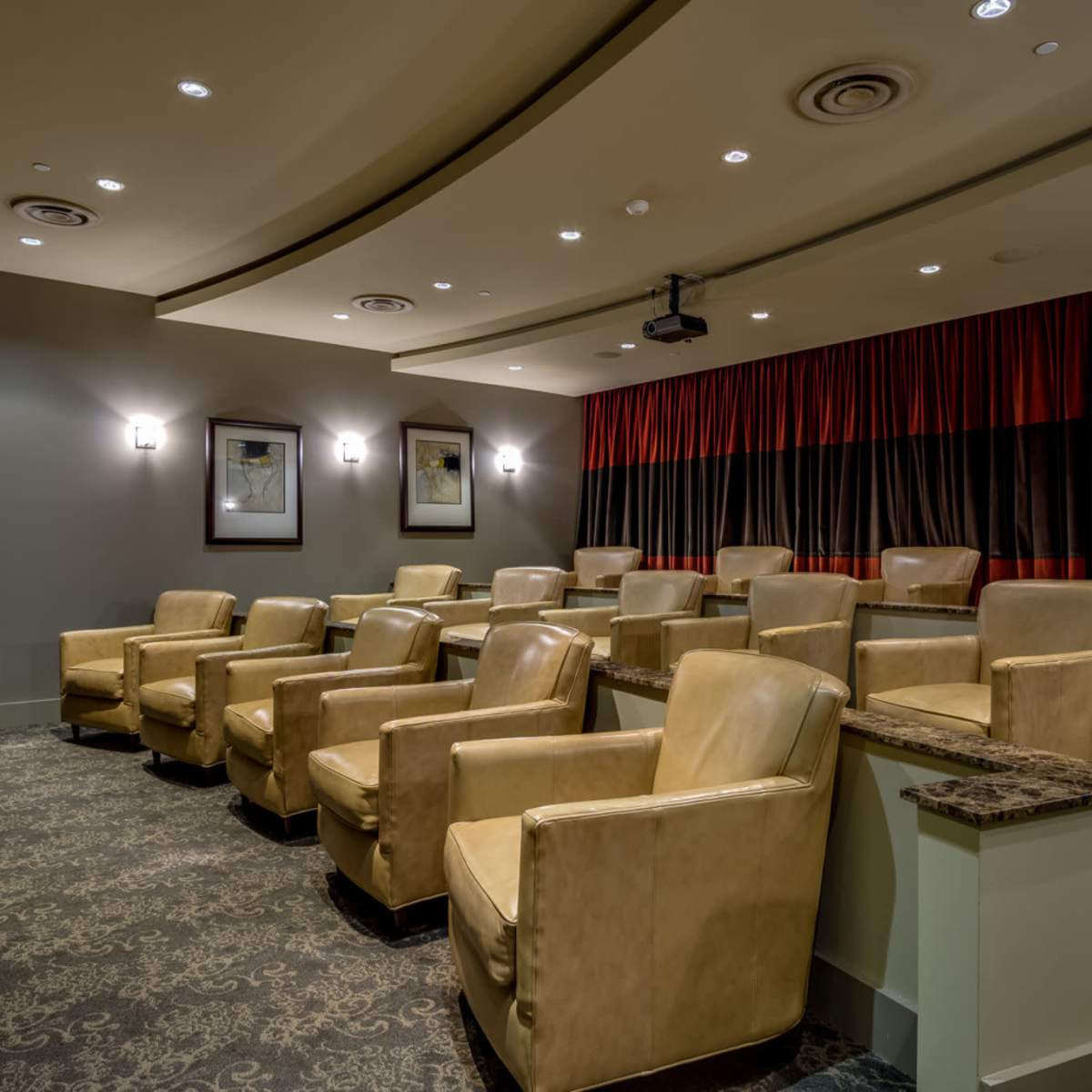 A dimly lit room designed for screenings, featuring rows of tan armchairs and a large projection screen.