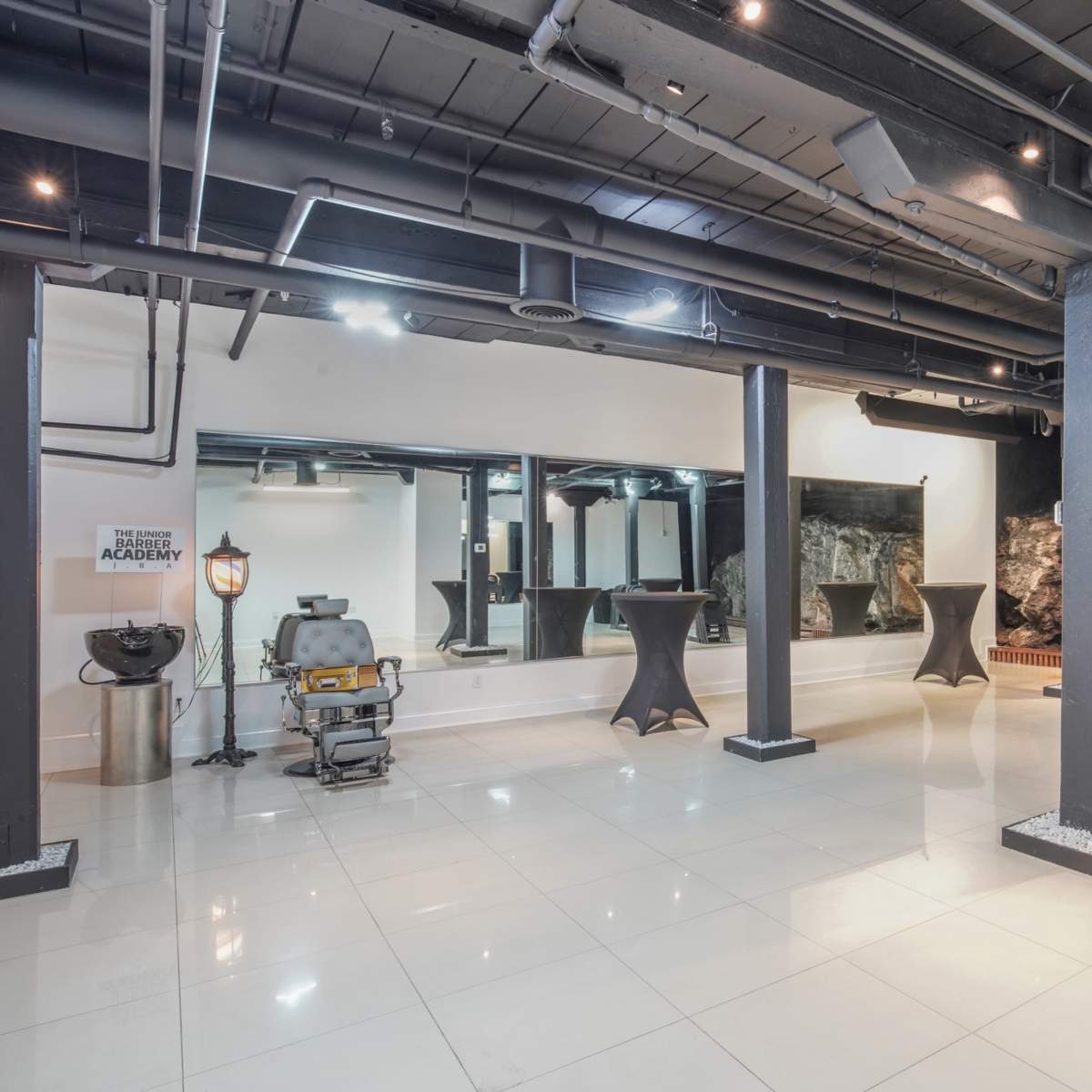 A spacious, modern venue with black columns, white tile flooring, and a rock feature wall, set up with several high tables.