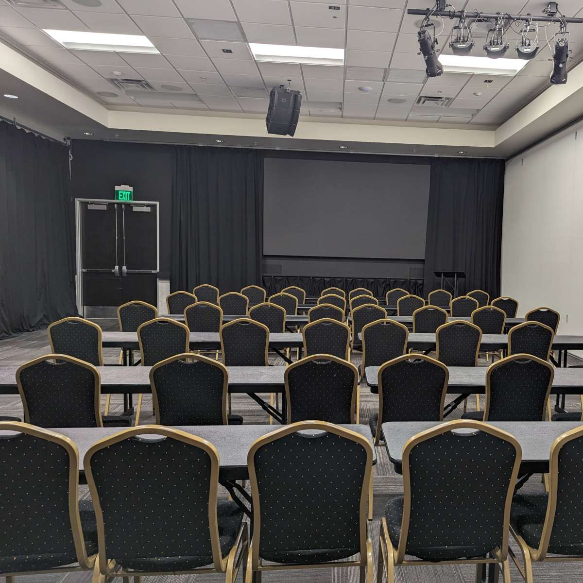 A conference room set up with rows of chairs and tables facing a large screen.