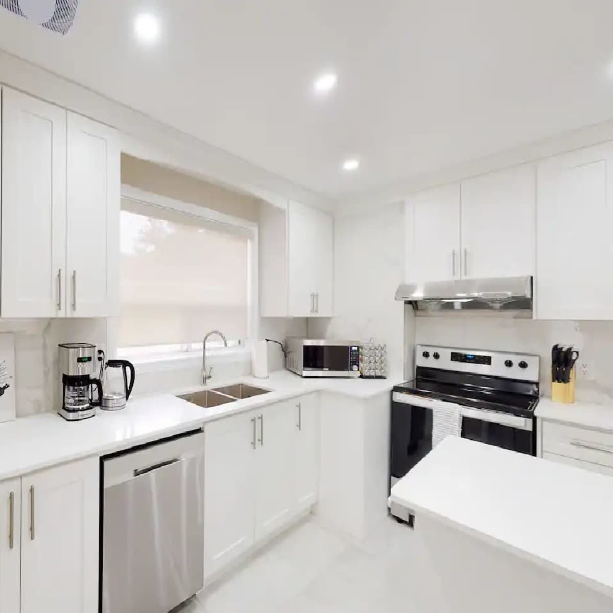 A modern kitchen features white cabinetry, stainless steel appliances, and a marble countertop with a double sink and a window above it.