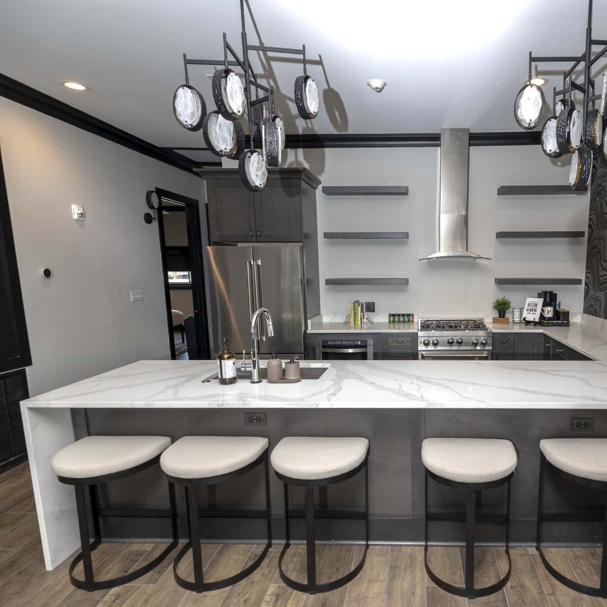 A modern kitchen with a marble countertop island, six bar stools, and decorative pendant lights above.