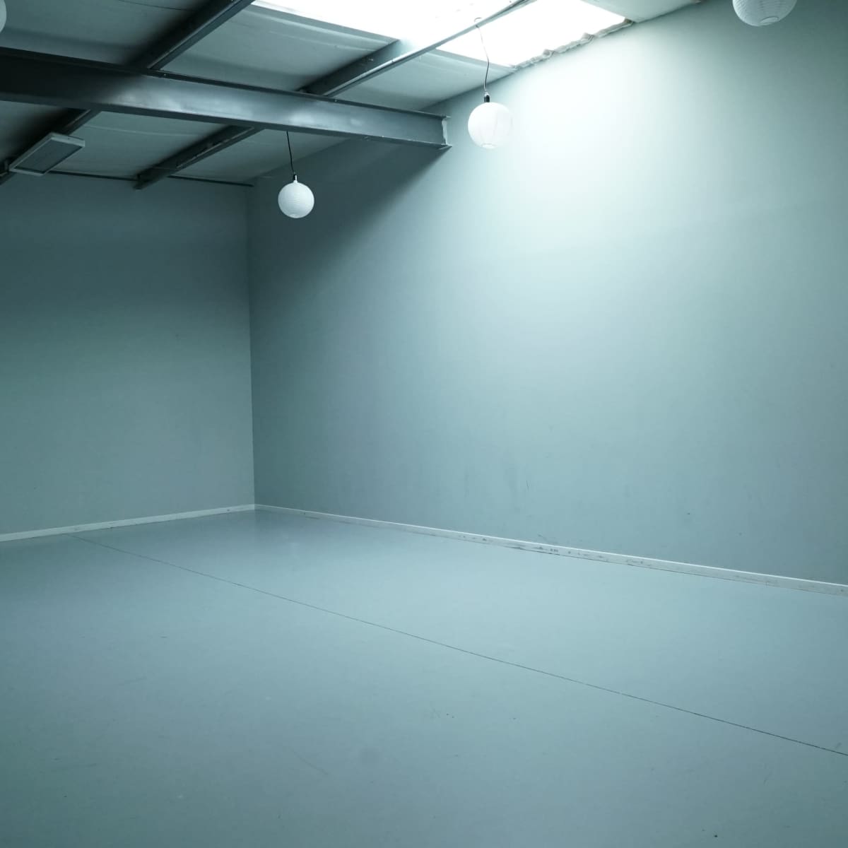 An empty room with a gray wall, concrete floor, and overhead light fixtures.