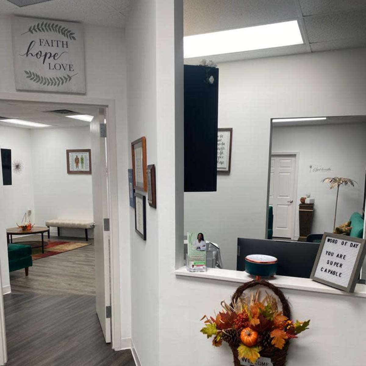 A bright hallway with framed artwork and a decorative basket of autumn leaves leads to a waiting area featuring green furniture.