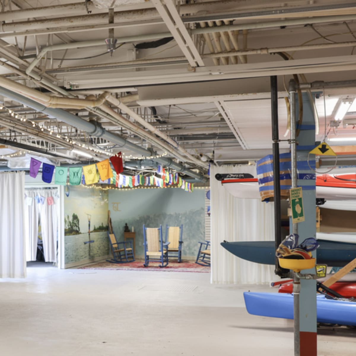 A spacious indoor area features several kayaks stacked along the walls and colorful banners hanging from the ceiling.