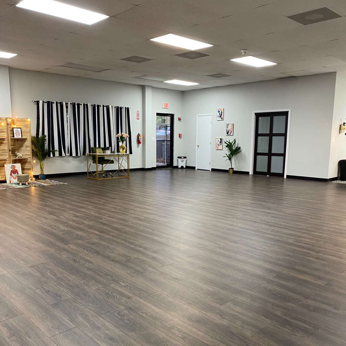 A spacious interior room with wood flooring, large windows, and a minimalistic design featuring chairs and decorative plants.