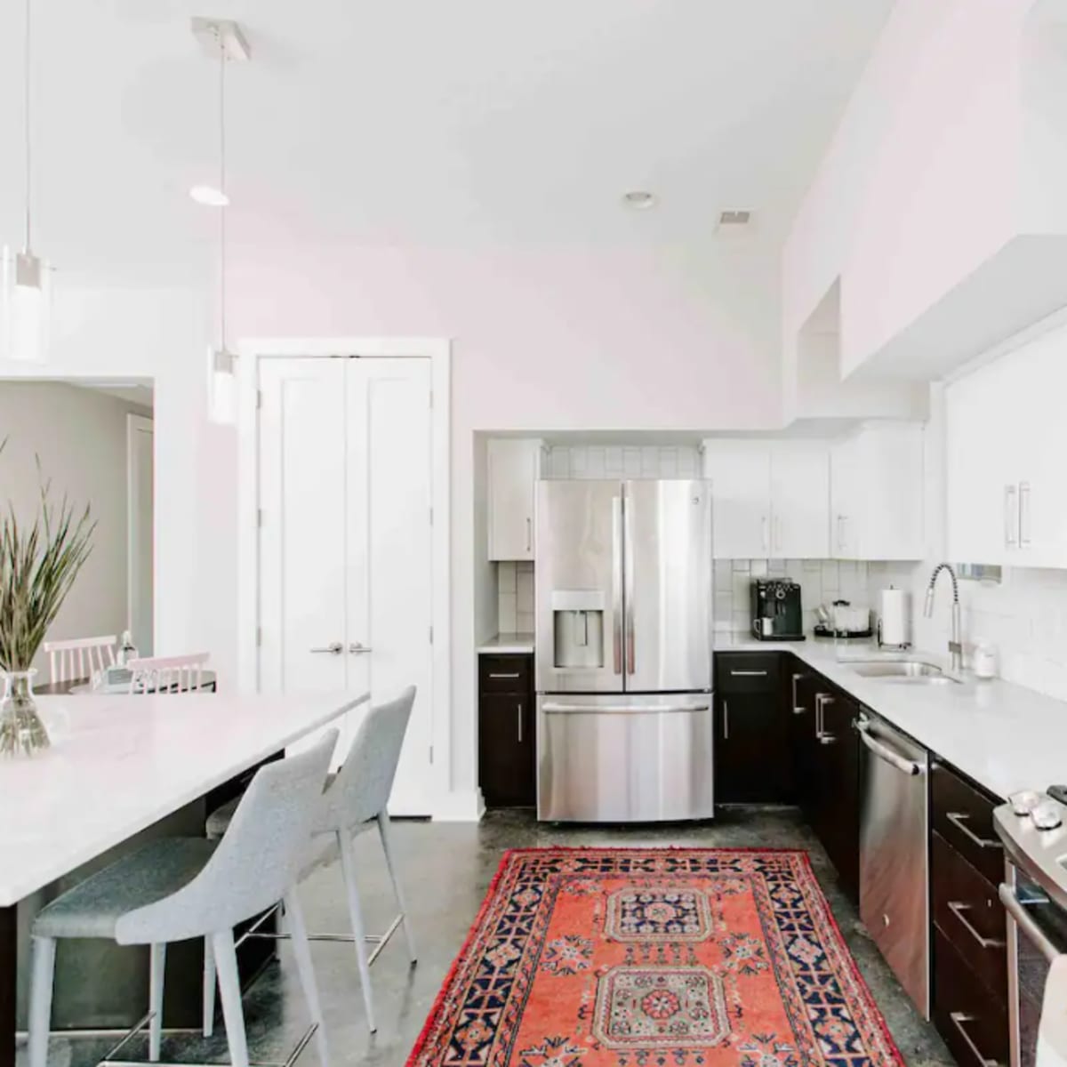 A modern kitchen features stainless steel appliances, white cabinetry, and a central island with bar seating, alongside a traditional patterned rug.
