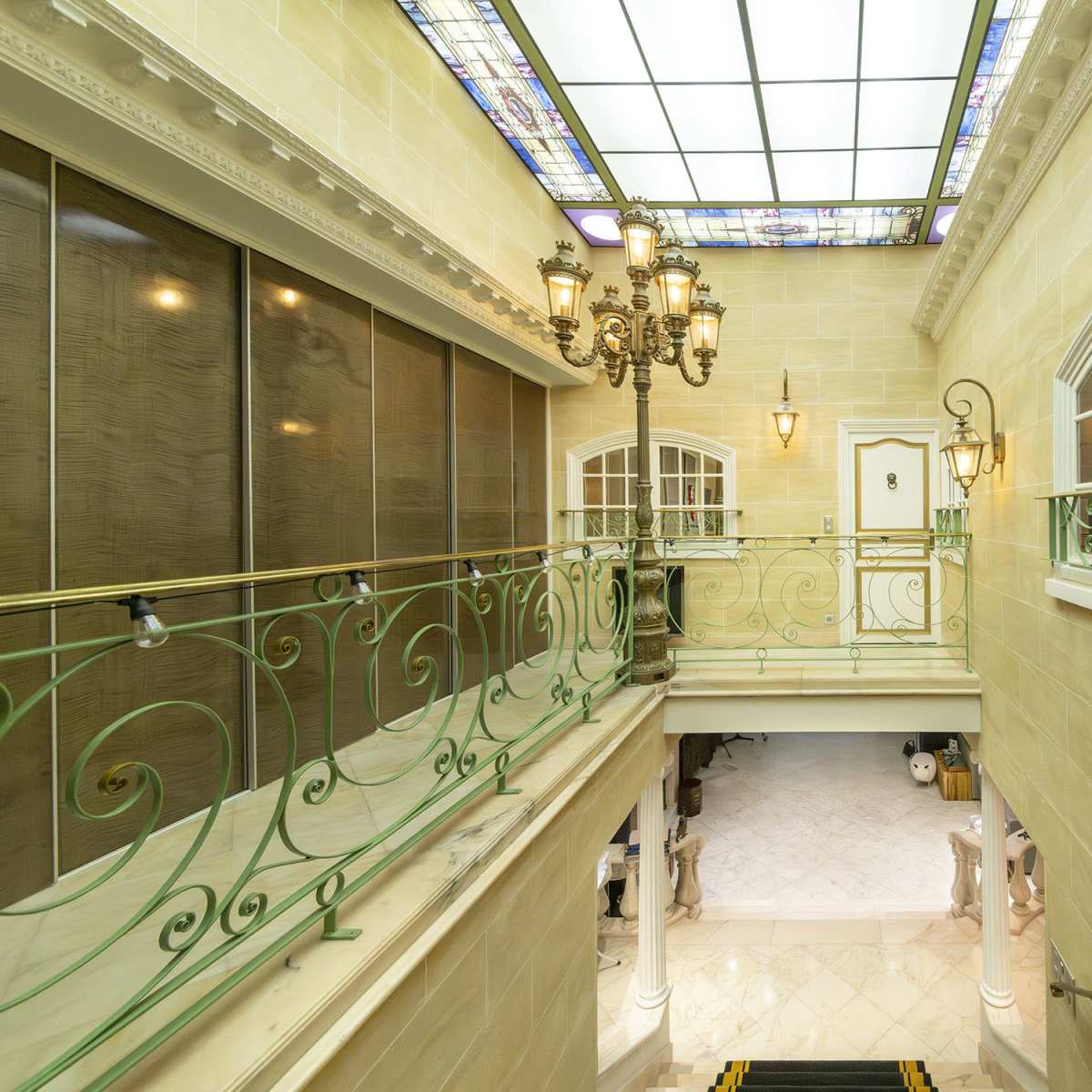 An elegant hallway with a staircase, decorative iron railing, and stained glass ceiling lights.