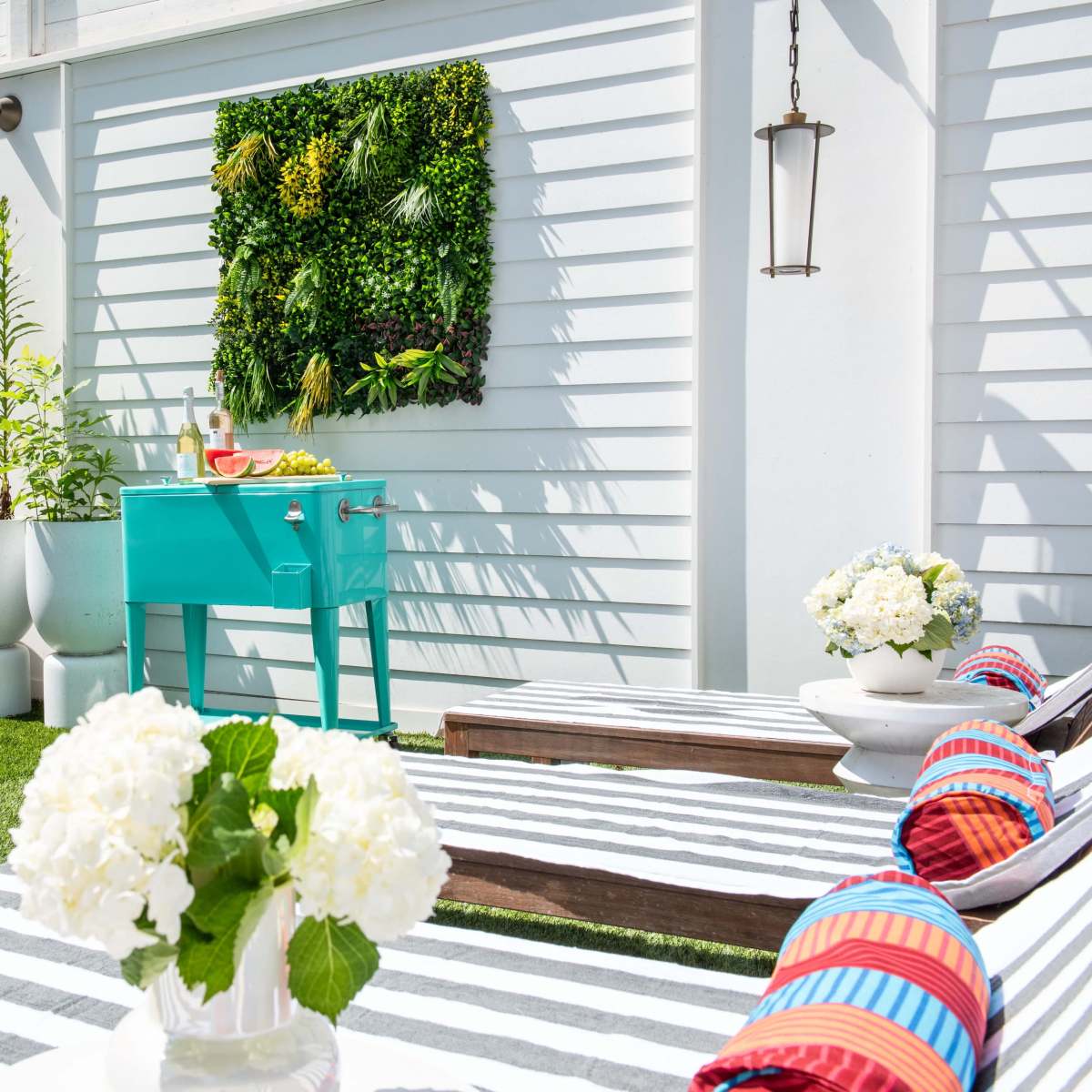 The scene features a modern outdoor space with lounge chairs, a turquoise grill, potted plants, and wall-mounted greenery beside a pool.