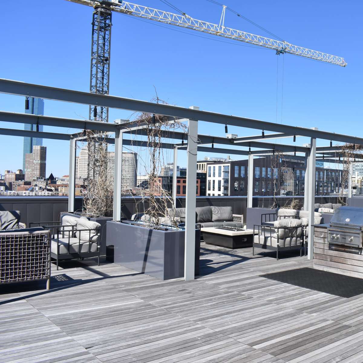 A rooftop deck featuring outdoor seating arrangements, barbecue grills, and a skyline view of a city under a clear blue sky.