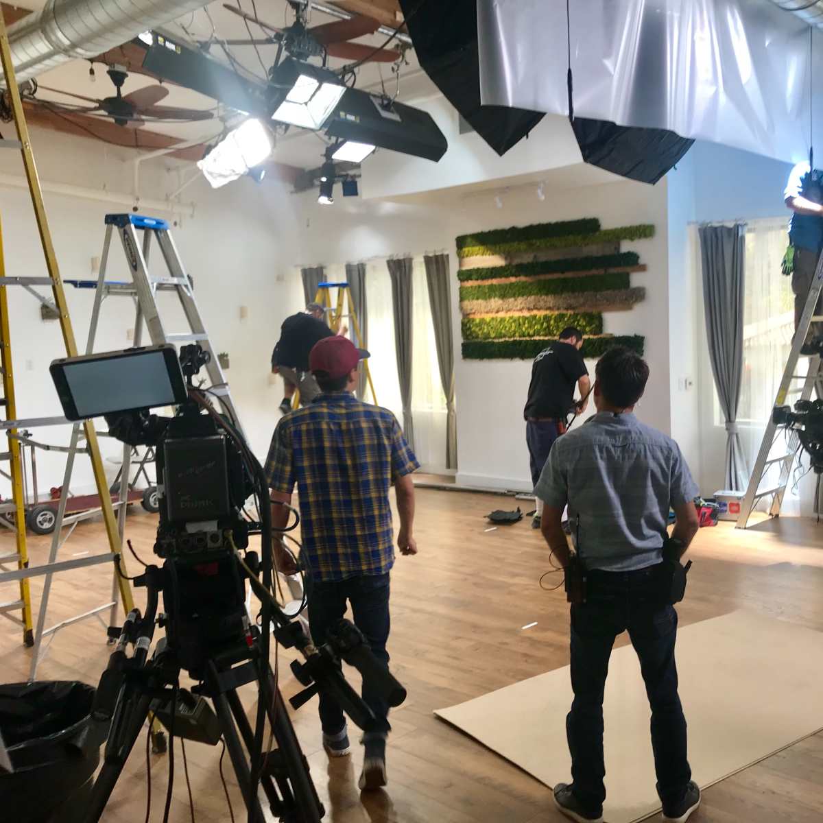 A film crew sets up equipment and lighting in a spacious interior for a production shoot.