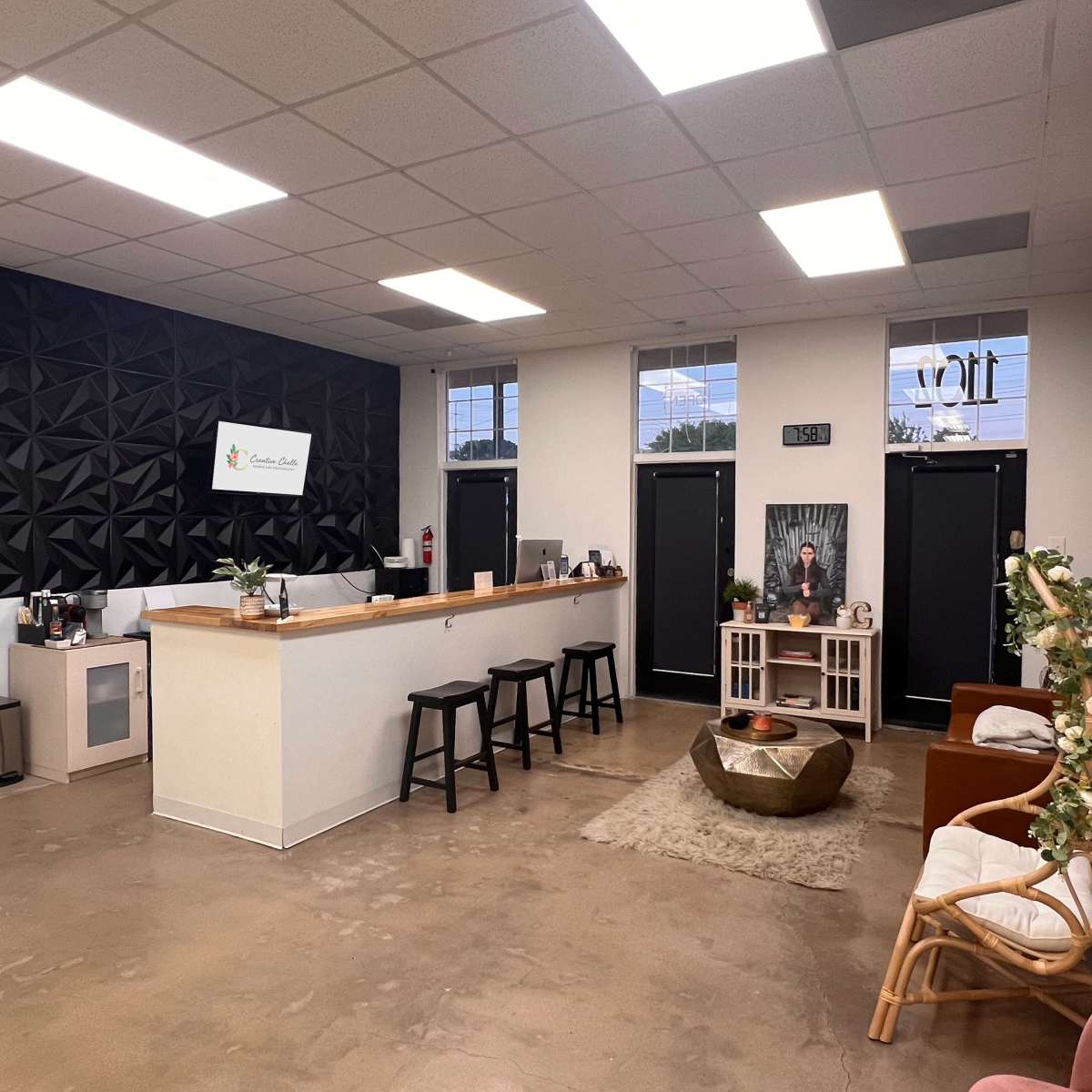 A modern reception area with a white service counter, several black stools, and a decorative seating arrangement featuring chairs and a rug.