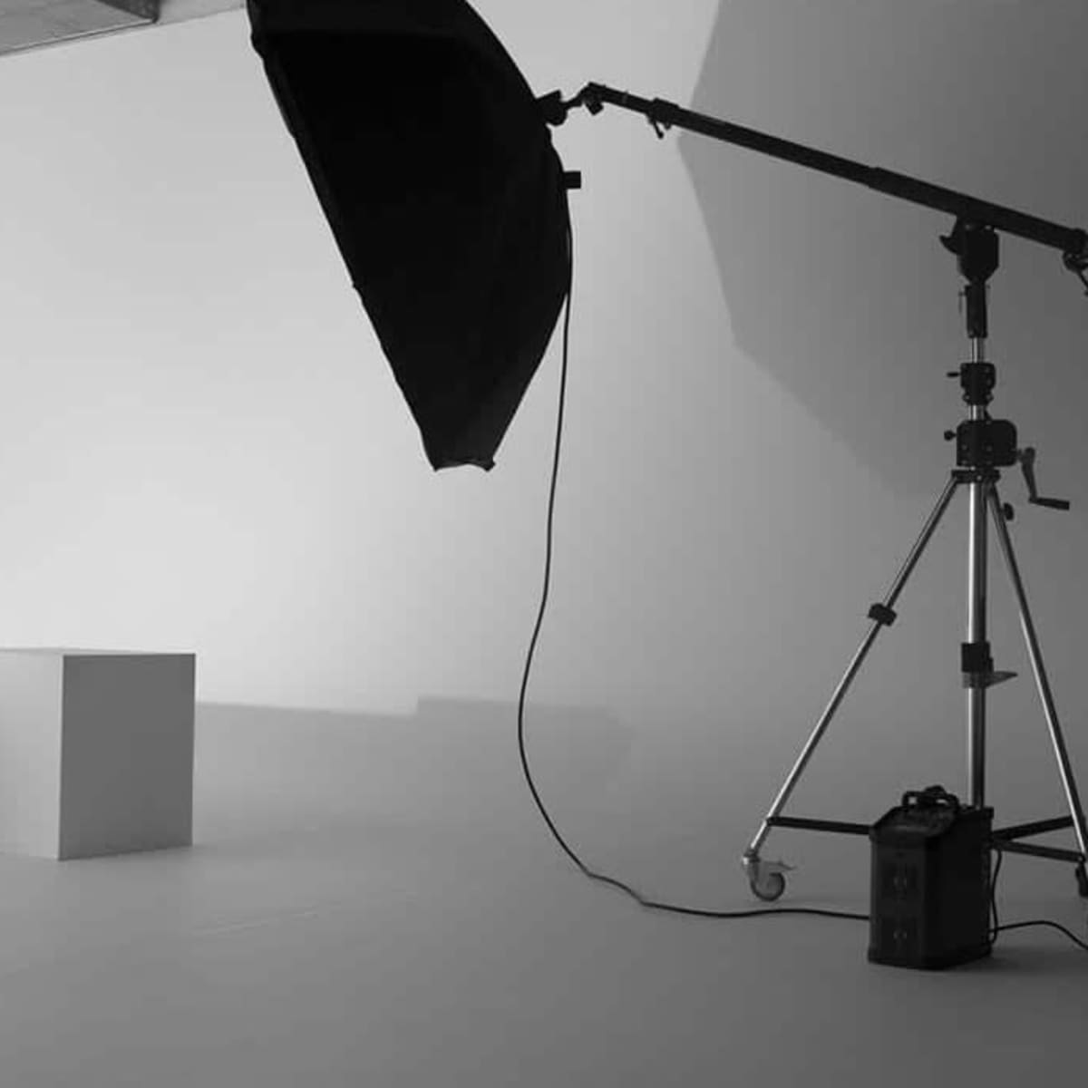 A minimalistic photography studio with two white cubes, a large softbox, and a light stand on a white backdrop.