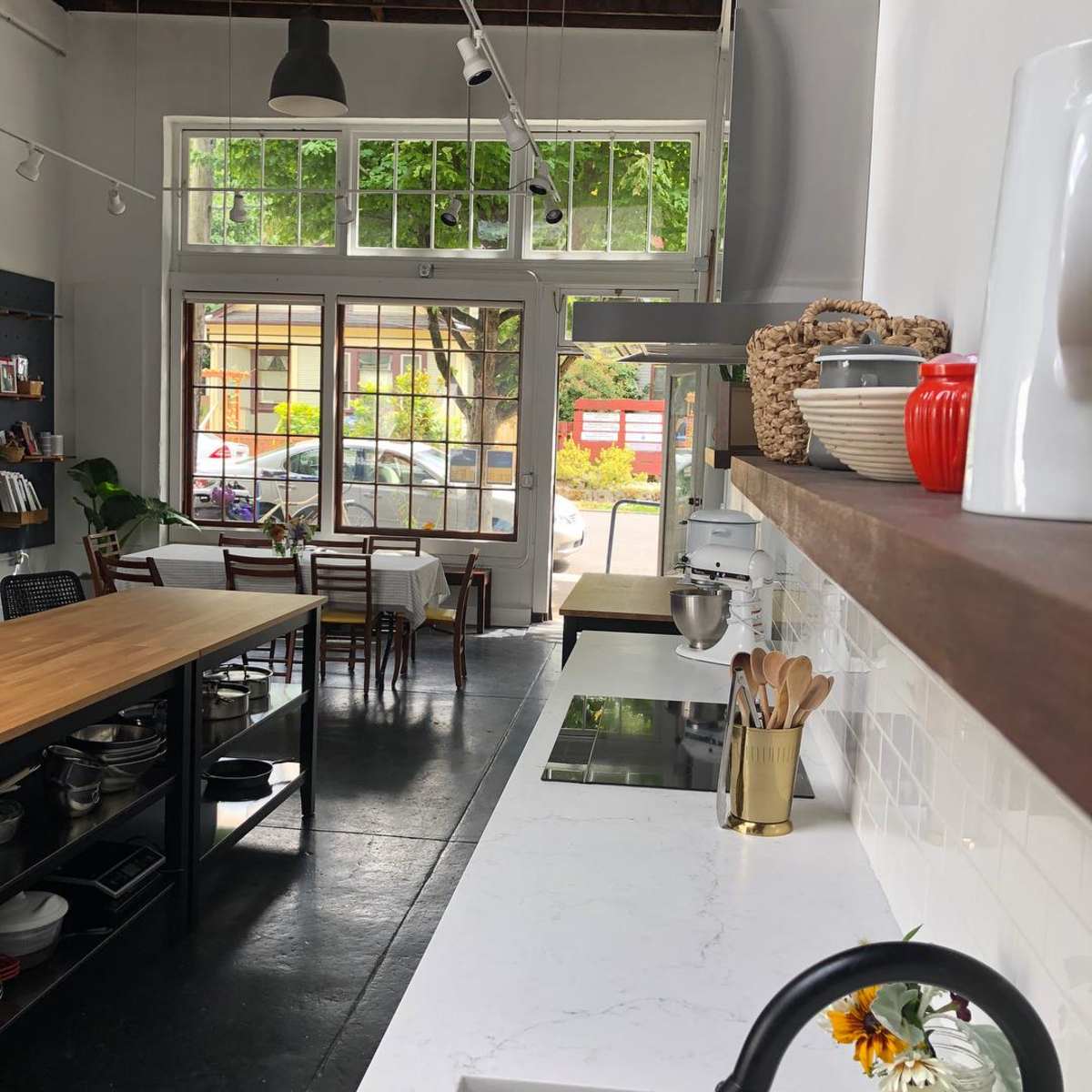 A modern kitchen features a countertop with cooking utensils and a large window overlooking a street with outdoor seating.
