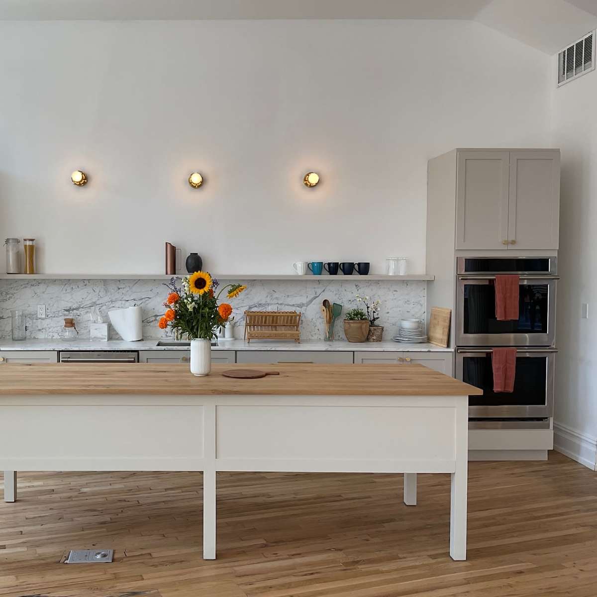 A modern kitchen features a central wooden island, stainless steel appliances, marble countertops, and a vase of sunflowers.