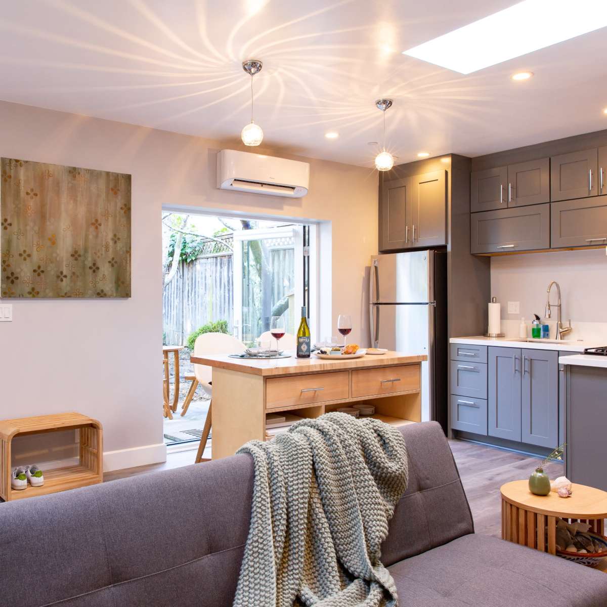 A modern kitchen and living area feature sleek cabinetry, open access to an outdoor space, and cozy furnishings.