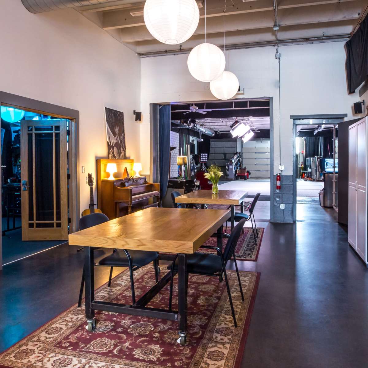A spacious studio-like interior with a wooden table, guitars leaning against the wall, and a series of round pendant lights hanging from the ceiling.
