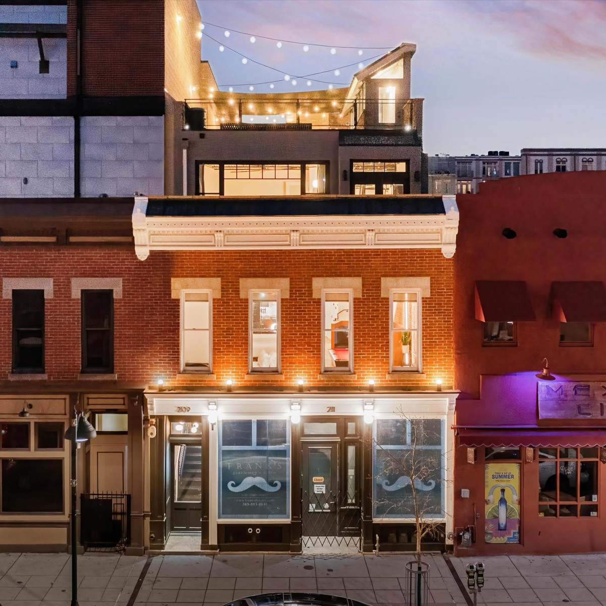 A street view of buildings illuminated at night, featuring a blend of historic architecture and modern lighting.