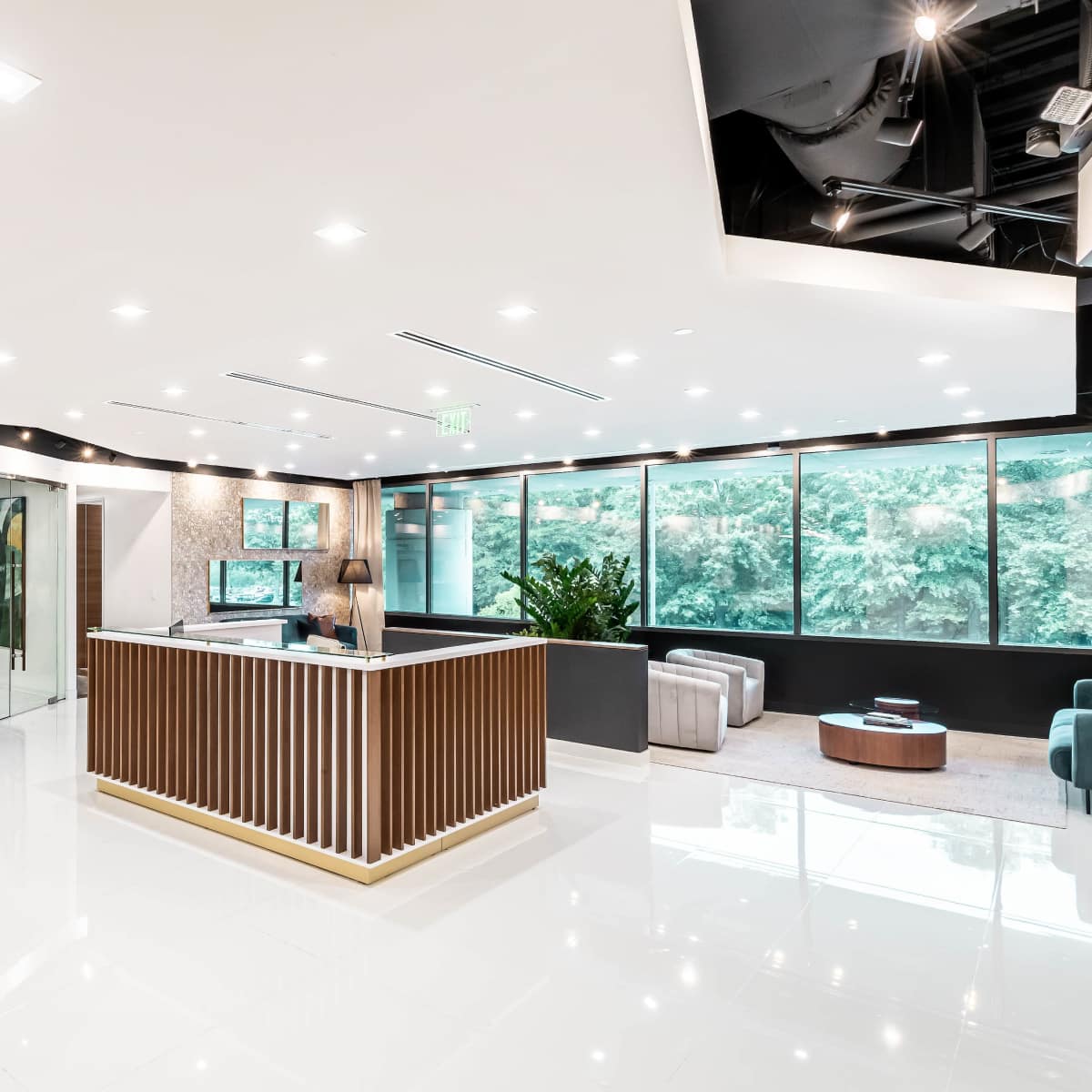 A modern reception area features a wooden front desk, sleek seating, and glass-walled meeting rooms surrounded by large windows.