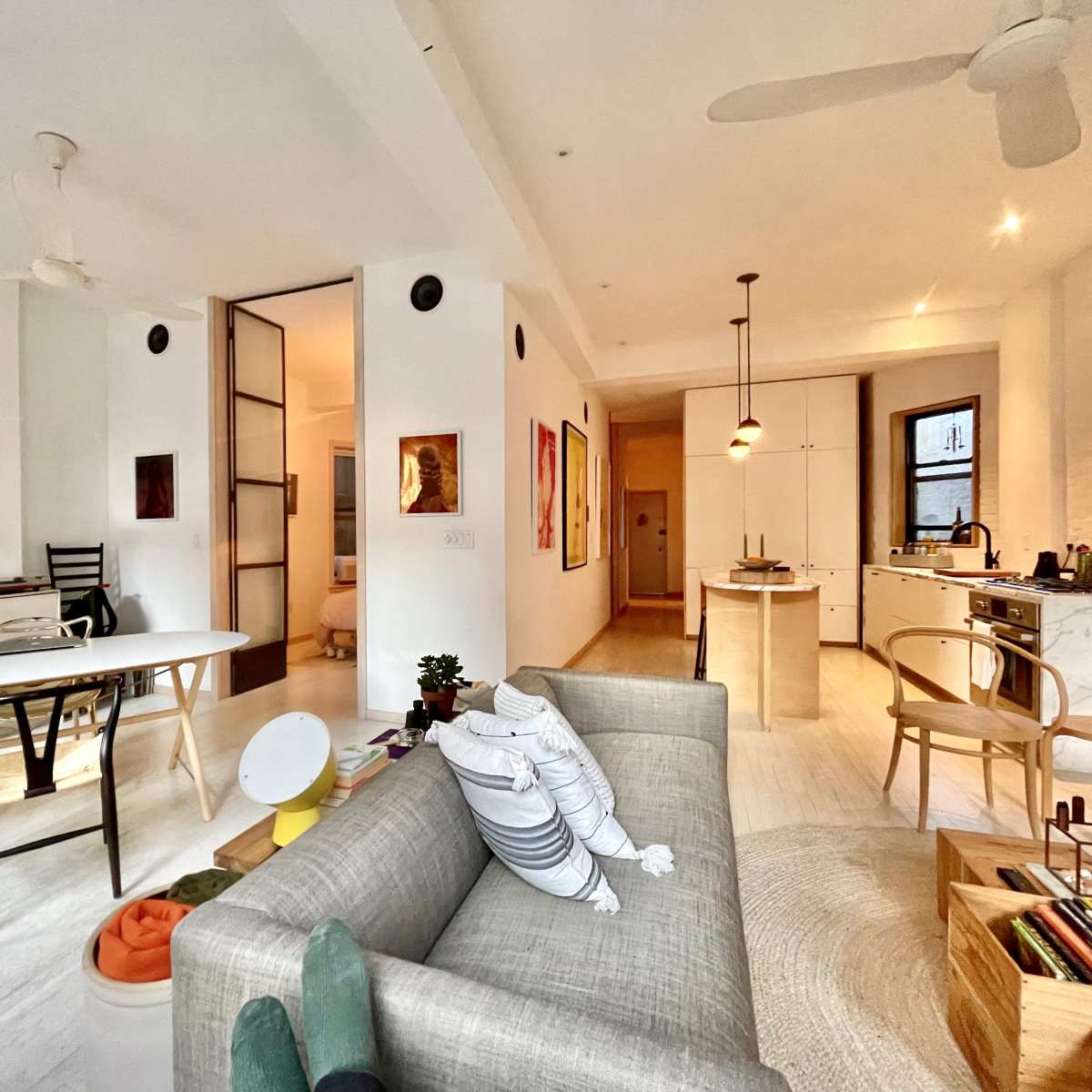 A modern, open-concept living space featuring a dining area, kitchen, and workspace arranged with minimalist furniture and decor.