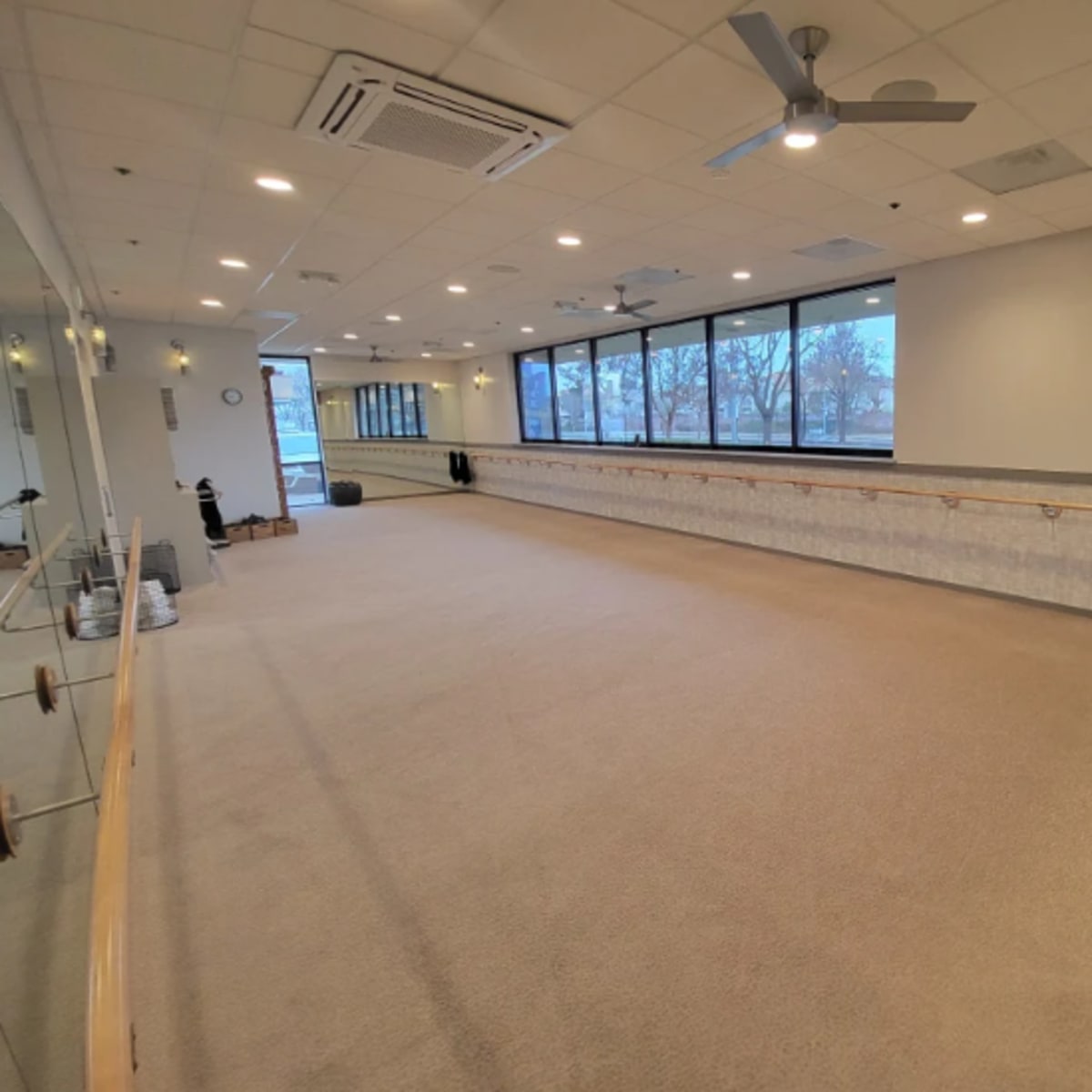 A spacious fitness studio with mirrored walls, a barre along one side, and large windows allowing natural light to fill the room.