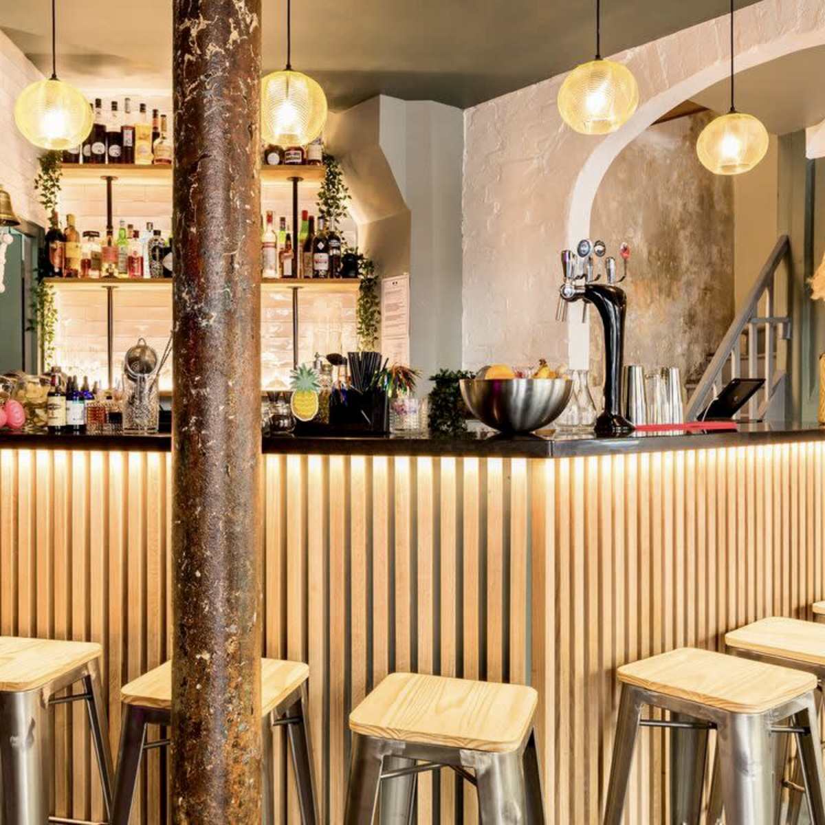 A bar area features a sleek counter with wooden paneling, adorned with pendant lights, and several metal stools arranged in front.
