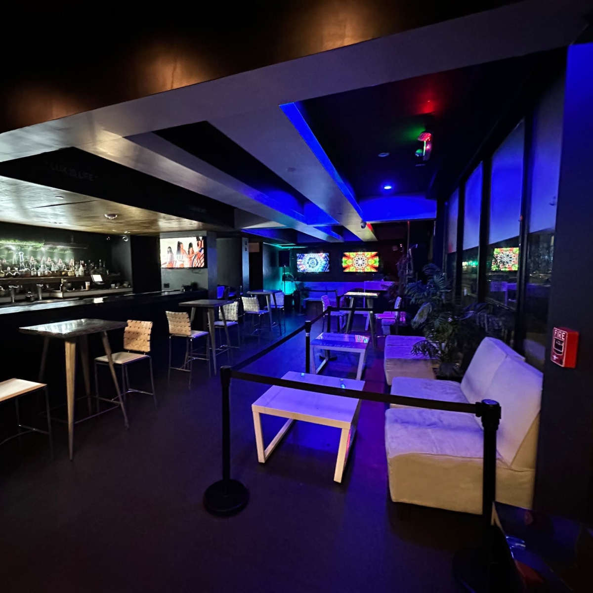 A dimly lit bar area with a sleek counter, a few tables and chairs, and vibrant neon lights illuminating the space.