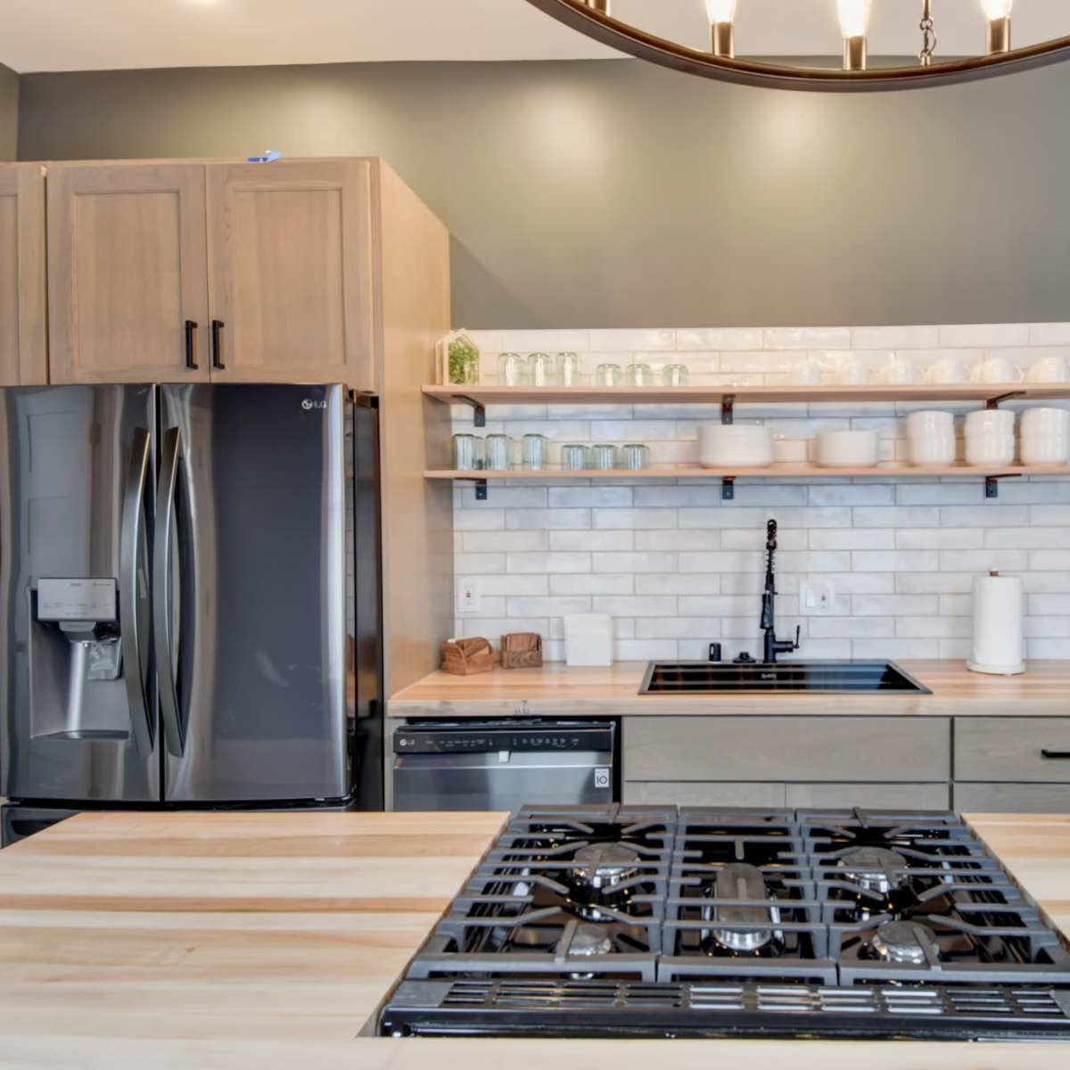 A modern kitchen with wooden cabinetry, a stainless steel refrigerator, and a gas cooktop featuring a black grill.