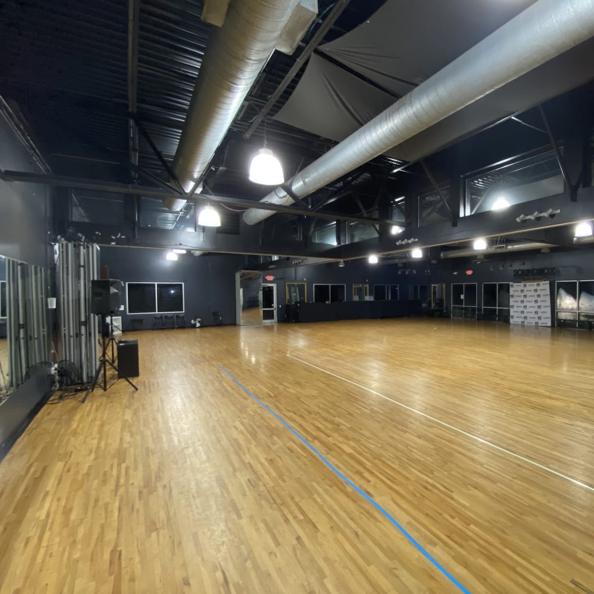 A spacious dance studio with wooden flooring, large mirrors, and high ceilings.