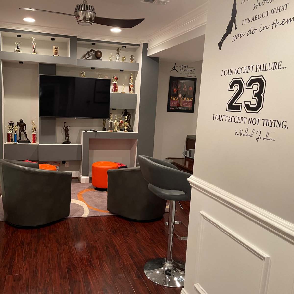 A well-decorated recreational room featuring a television, trophies, a small basketball hoop, and seating arranged around an orange and gray carpet.
